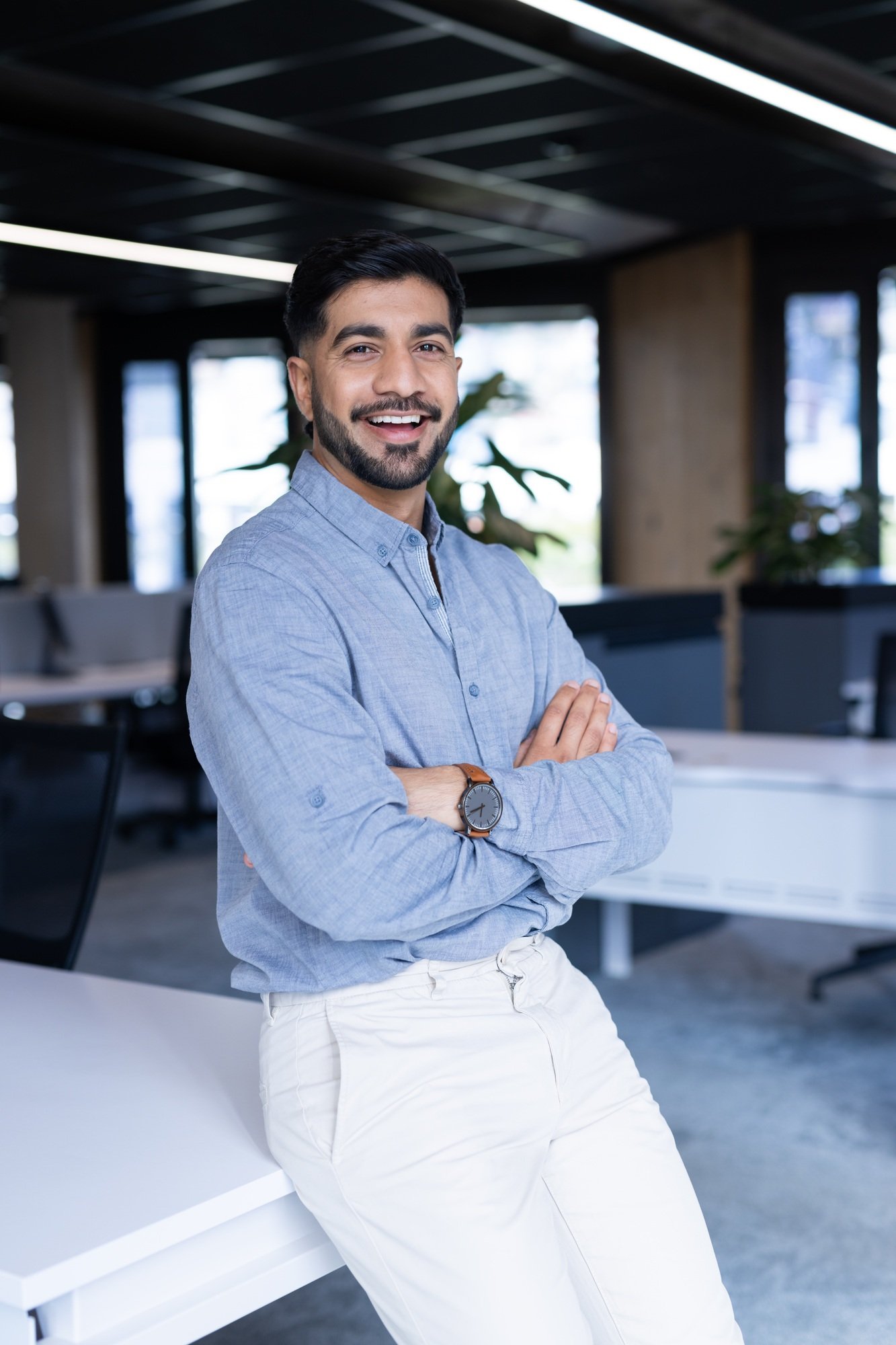 Smiling businessman in modern office, standing with arms crossed confidently